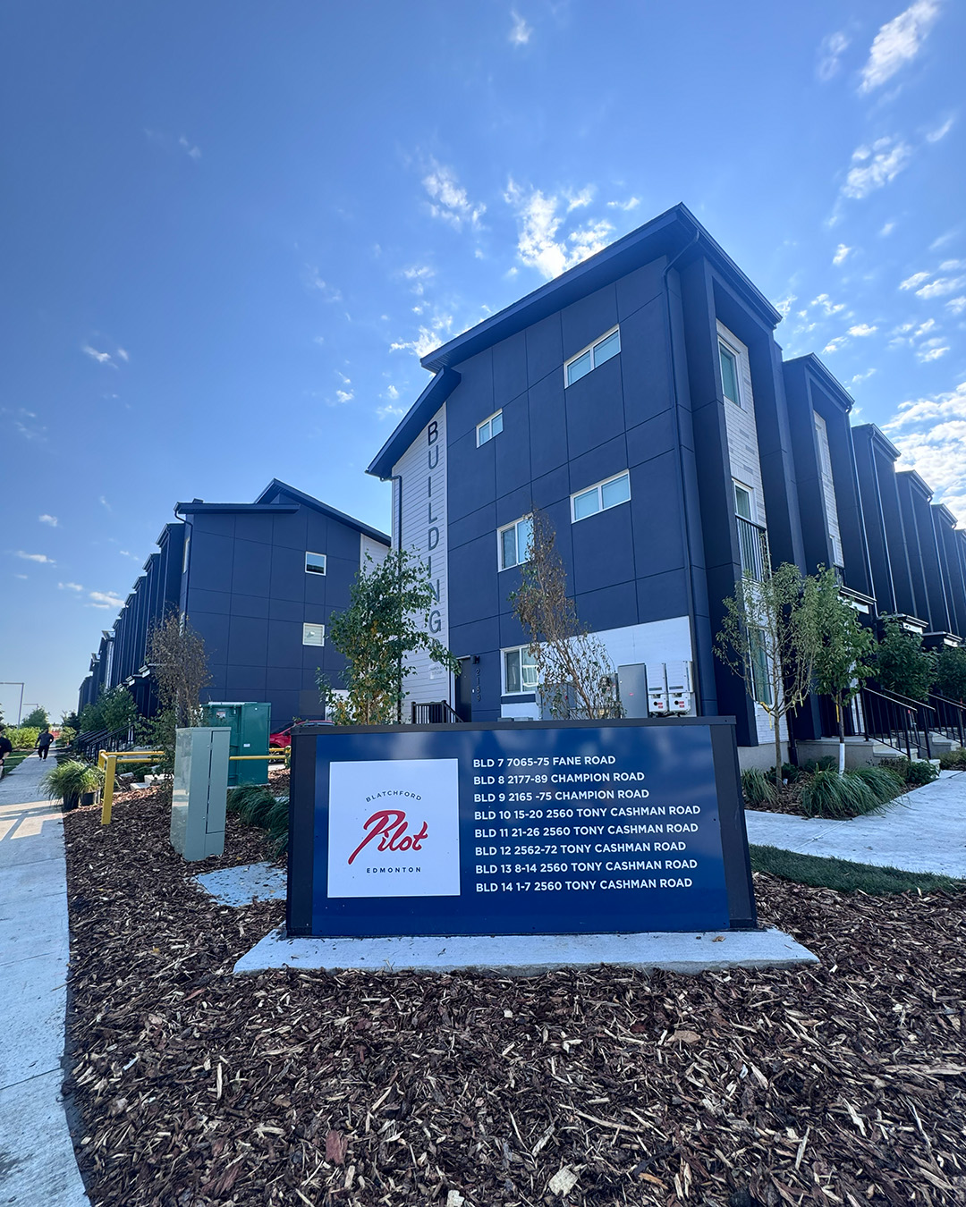 Exterior view of Pilot townhome development with large 'welcome'/directional sign in front.