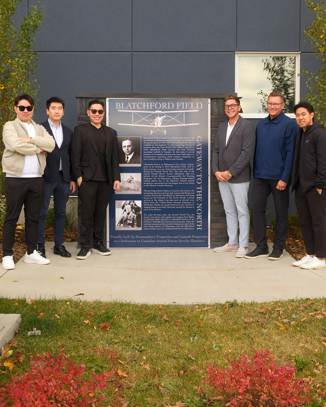 Three men stand on each side of the commemorative plaque.