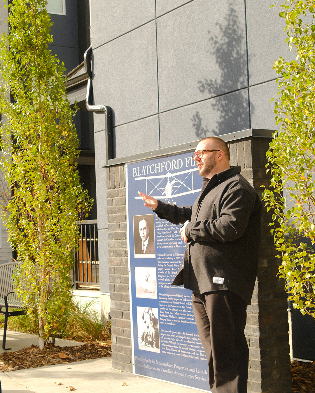 A man speaks to a crowd while standing next to the commemorative plaque.
